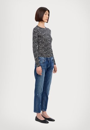 Haut à manches longues avec un motif noir et blanc ; jeans en denim bleu à coupe décontractée avec un léger effet usé ; chaussures plates noires.