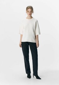 Un haut oversized blanc à manches courtes, accompagné d'un pantalon en denim noir coupe droite et de chaussures à talons aiguille noires. Design simple et épuré.