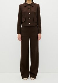 Brun skräddarsydd kostym med en kort blazer med rundad krage, två framfickor och silverknappstängning; vida byxor.