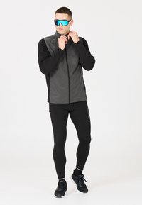 Svarta träningsleggings och en åtsittande grå väst med hög krage. Utrustad med blå reflexglasögon, texturerat tyg och en slank design.