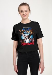 Schwarzes T-Shirt mit einem grafischen Druck des Charakters Gizmo aus "Gremlins" und anderen Kreaturen. Text über dem Grafikdruck in Weiß.