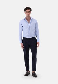 Camicia azzurro chiaro con colletto classico, abbinata a pantaloni navy sartoriali e mocassini in pelle scura. Texture liscia, design aderente.