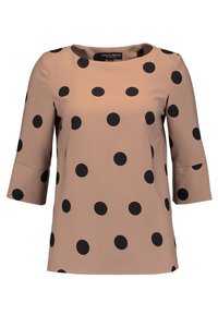 Beige blus med svarta prickar, trekvartslånga ärmar och rund halsringning.