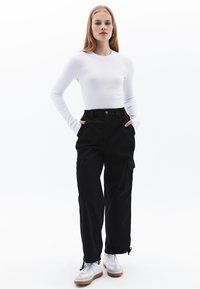 Svarta cargo-byxor med sidofickor, elastisk midja och dragsko i fållen. Matchas med en vit långärmad tajt topp och vita sneakers.