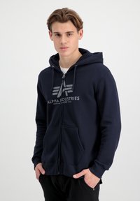 Hanorac închis la culoare, cu fermoar, dintr-un amestec de bumbac, având un imprimeu cu logo pe partea din față, două buzunare, glugă cu șnur și mansete ribbate.