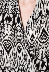 Czarna i biała sukienka kopertowa z geometrycznym wzorem, wykonana z miękkiej, teksturowanej tkaniny oraz z głębokim dekoltem.