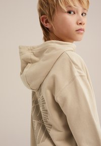 Beiger Hoodie mit einer weichen Textur, auf dem Rücken mit einem grafischen Design. Die Kapuze ist leicht lässig, mit sichtbaren Stichdetails.