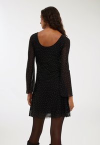 Czarna sukienka z długimi, przezroczystymi rękawami i dekoltem w serek, ozdobiona małymi srebrnymi kropkami, charakteryzująca się luźnym krojem i lekkim materiałem.