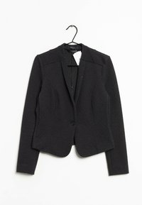 Blazer nero con texture, caratterizzato da un design aderente, colletto a punta, chiusura con un bottone e spalle strutturate. Appeso a un gancio.