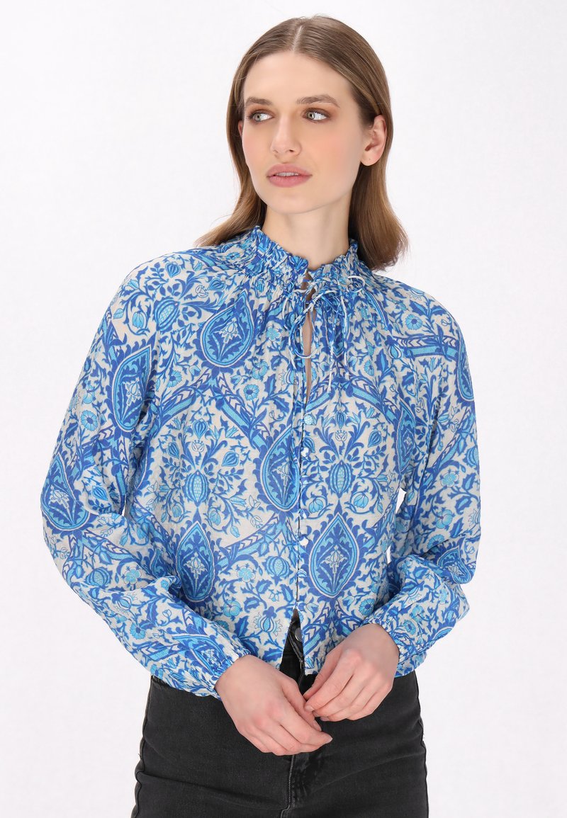 Blaue gemusterte Bluse mit gerafftem Ausschnitt, Knopfverschluss und langen Ärmeln, die ein Paisleymuster auf hellem Hintergrund zeigt.