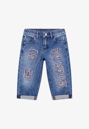 Pantalon en denim bleu pour tout-petits avec taille élastique, revers roulés et écussons cousus formant le mot « GUESS » sur les jambes avant.
