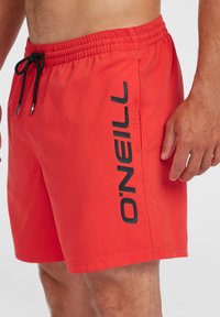 Piros fürdőnadrág fekete húzózsinórral, a oldalán kontrasztos fekete "O'Neill" logóval. Könnyű anyagból készült, sima tapintású.