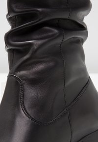 Bota de cuero negro con un diseño arrugado que presenta una textura plegada, costuras sin costura y un acabado suave y brillante. Tacón bajo.