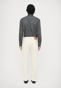 Koszula z kołnierzem w czarny wzór, białe spodnie o prostych nogawkach oraz czarne buty, z wycięciem ze skóry na tylnej części pasa spodni.