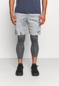 Pantalones cortos atléticos grises con un patrón texturizado, combinados con leggins gris oscuro que presentan un diseño elegante y zapatillas Nike negras.