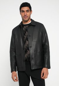 Schwarze Lederjacke mit Kragen, zwei Vordertaschen und Knopfverschluss, kombiniert mit einem gemusterten Pullover darunter.