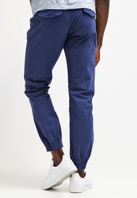 Námorně modré bavlněné jogger kalhoty s elastickými manžetami, které mají boční kapsy a hladkou texturu. Nosit s bílými teniskami.