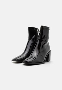 Bottines en cuir verni noir avec un côté pointu, fermeture éclair sur le côté et un talon bloc texturé. Fini lisse et brillant avec un design élégant.
