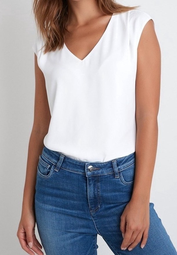 Femme portant un haut blanc sans manches en V rentré dans un jean en denim bleu taille haute sur un fond uni.