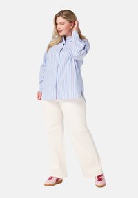 Chemise boutonnée à rayures bleu clair et rose avec des manches longues, associée à un pantalon large blanc et des baskets roses avec des accents rouges.