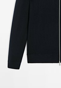 Svart zippered cardigan med långa ärmar, ribbade muddar och fåll, tillverkad av ett mjukt stickat material som har en slät yta och silverdragkedja.