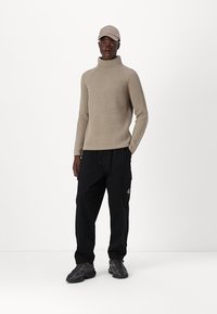 Beige gerippter Rollkragenpullover, schwarze Cargo-Hosen mit Seitentaschen und graue Sneakers mit strukturiertem Design. Lässiger Streetwear-Look.