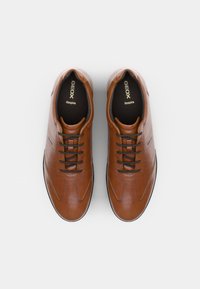 Brown leather lace-up shoes with contrasting black laces, smooth texture, rounded toe, and a subtle geometric pattern on the sides.