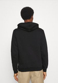 Schwarze Kapuzenjacke mit weicher Textur, ausgestattet mit einer großen Kapuze und gerippten Bündchen. Entworfen mit einem lässigen Schnitt, kombiniert mit beigen Hosen.
