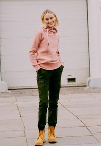 Różowa bluza z kapturem i sznurkiem, czarne spodnie cargo z bocznymi kieszeniami i beżowe buty na sznurówki. Prosty design, casualowy wygląd na świeżym powietrzu.