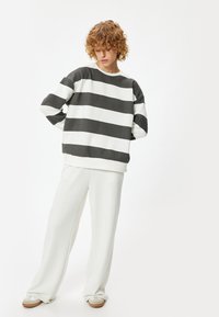 Felpa a righe grigie e bianche con una vestibilità ampia e scollo rotondo, abbinata a pantaloni bianchi a gamba larga e sneakers chiare.
