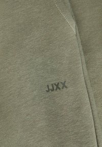 Olívovo zelená bavlnená mikina so zreteľným logom "JUXX" v čiernej farbe. Tkanina má jemnú textúru s hladkým povrchom.