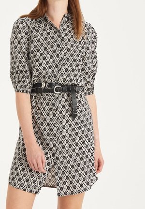 Robe à manches courtes avec un motif floral noir et blanc, col avec col, et une ceinture noire ornée de clous et d'une boucle.