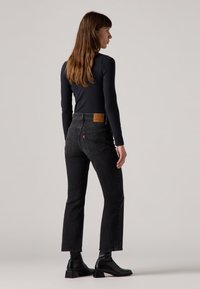 Zwarte high-waisted jeans met een rechte pijp, voorzien van een leren label op de achterkant, gedragen met een zwart lange mouwen top en enkellaarsjes.