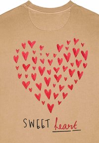 Felpa beige con un grande design a forma di cuore composto da tanti piccoli cuori rossi. Testo "SWEET heart" ricamato in nero e rosso sotto il cuore.
