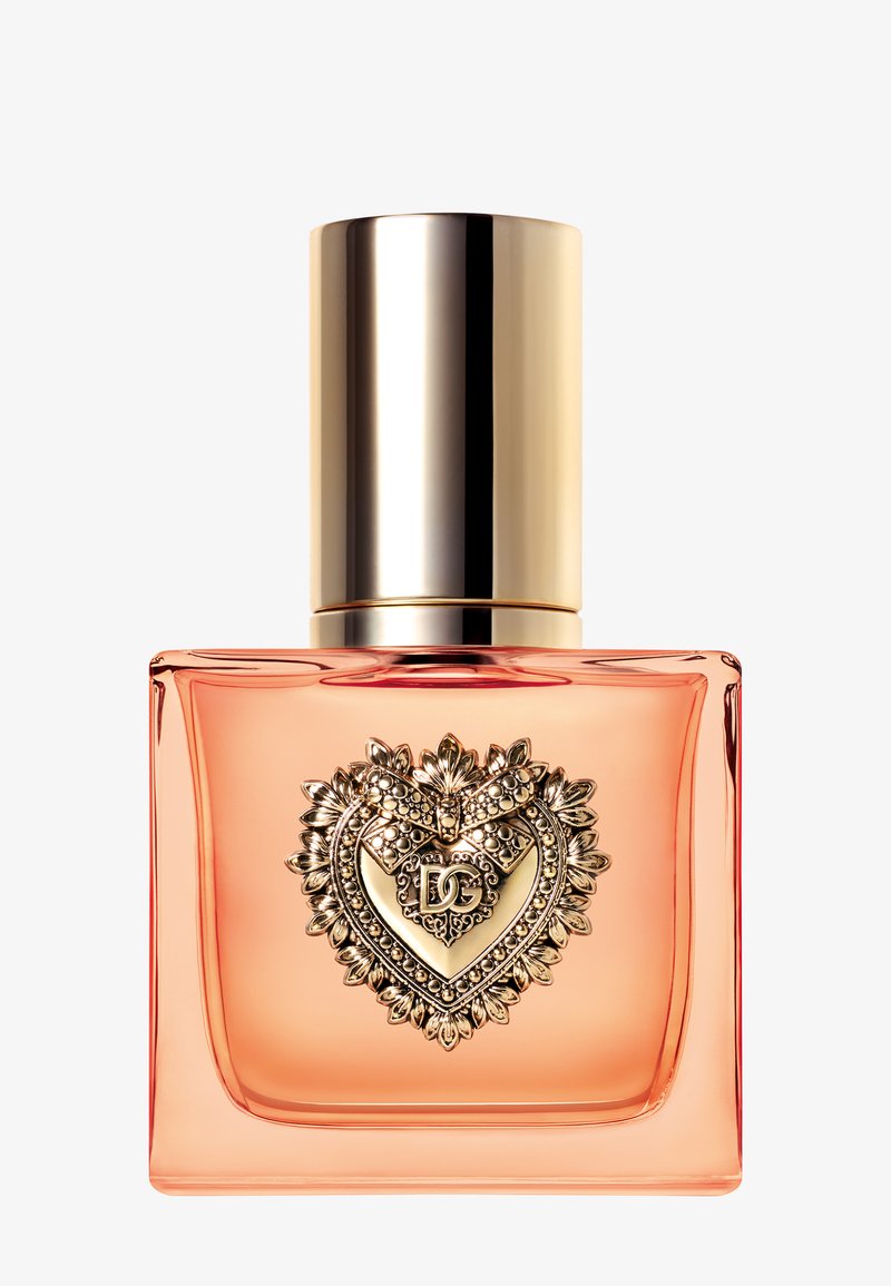 Bottiglia di profumo quadrata in vetro con liquido color pesca, emblema decorato a forma di cuore dorato e tappo dorato lucido.