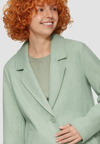 Mintgroene wollen blend jasje met opstaande kraag, enkele knopen sluiting en zijzakken. Geribde groene top zichtbaar eronder.
