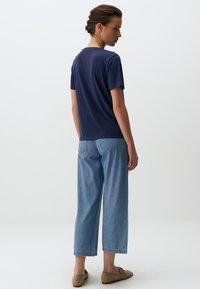 Marineblauwe t-shirt met een ronde hals, gecombineerd met lichtblauwe cropped denim broek. Model draagt beige instappers.