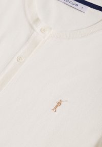 Bílý cardigan vyrobený z měkkého materiálu, se zaobleným výstřihem a pěti knoflíky. Obsahuje malé zlaté vyšívané logo na hrudi.