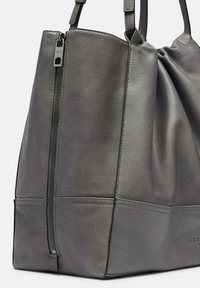 Graue Leder-Tote mit einem gerafften Oberteil, einem mit Reißverschluss gesicherten Hauptfach und dezenten genähten Details entlang der Unterseite.