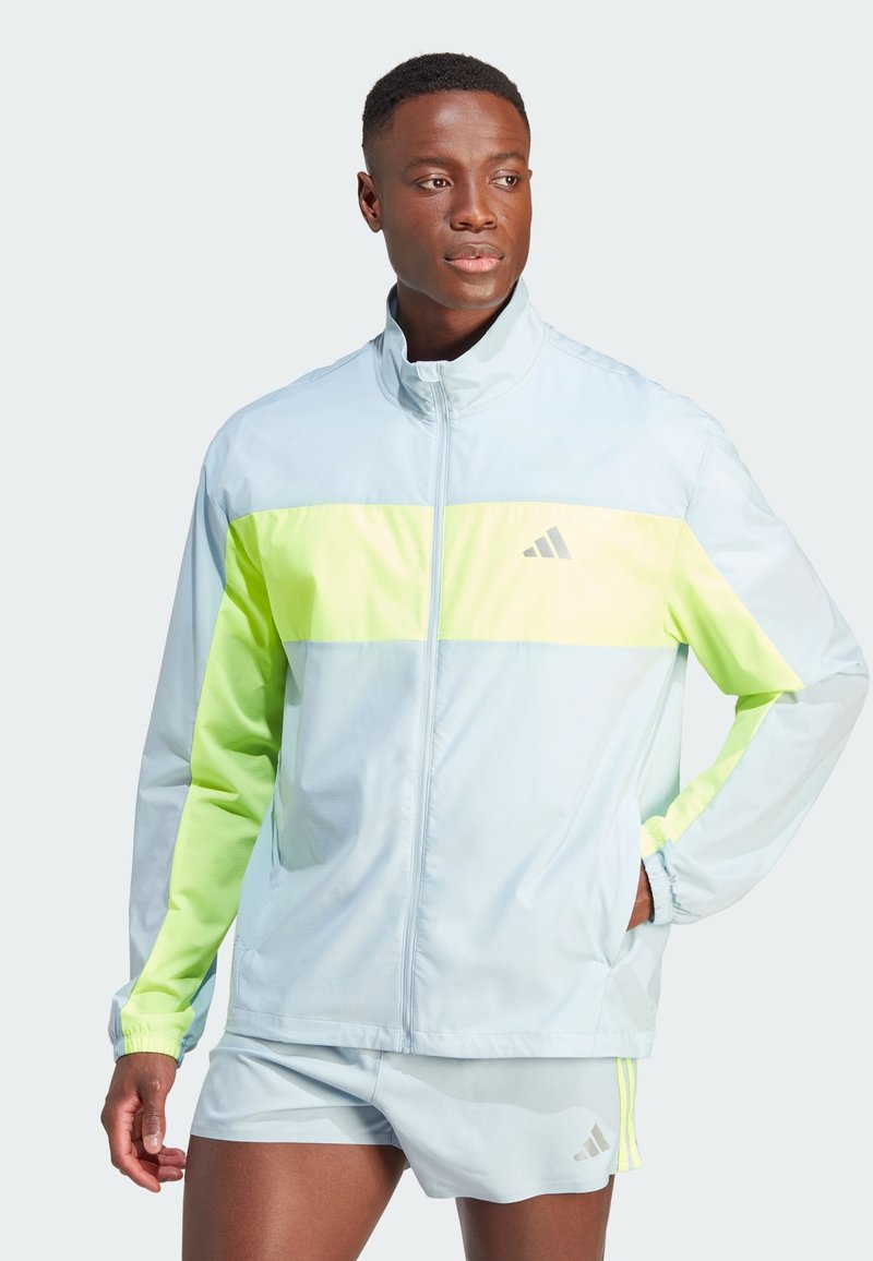 Himmelblaues Sportjacke mit einem leuchtend gelb-grünen horizontalen Streifen, Reißverschlussverschluss und Adidas-Logo auf der Brust. Lange Ärmel, leichtes Material.