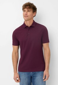 Polo shirt bordeaux a maniche corte realizzato in cotone liscio, con colletto classico e placca con tre bottoni, abbinato a jeans in denim chiaro.