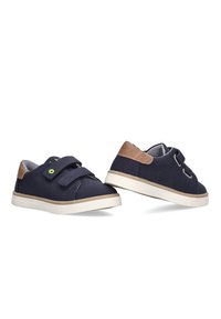 Zapatos de lona azul marino con acentos en color tan, correa de Velcro ajustable, suela de goma blanca y forro interior a rayas.