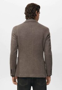 Blazer marrone a motivo houndstooth con reverse, taglio strutturato e polsini con bottoni; tessuto texturizzato con un motivo sottile.