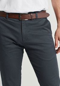 Pantaloni grigio antracite con una finitura testurizzata, e una cintura in pelle marrone con una fibbia in metallo argentato, indossati con una camicia bianca.