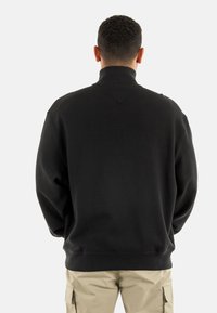 Sudadera nera a trama con colletto alto, vestibilità comoda e polsini in costina. Indossata con pantaloni cargo beige.