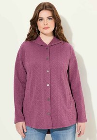 Lila, texturerad jacka med spetsig huva, med knäppning fram och två sidofickor. Designen inkluderar ett diamantmönster.