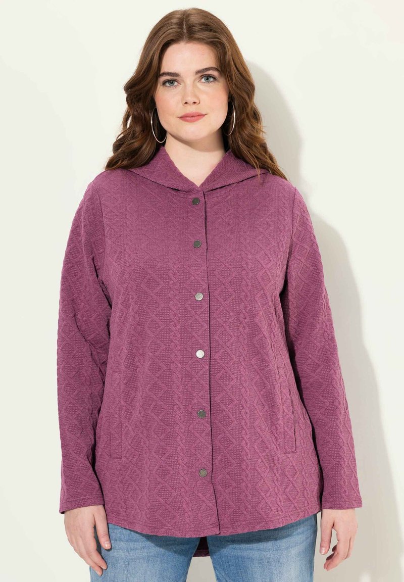 Lila, texturerad jacka med spetsig huva, med knäppning fram och två sidofickor. Designen inkluderar ett diamantmönster.