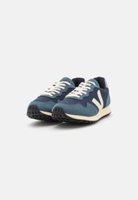Blue and gray sneakers with textured mesh and suede upper, cream laces, white logo accents, and a black rubber sole.