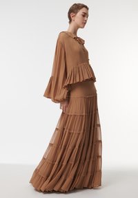 Robe longue et marron à volants avec un haut assorti, comprenant des couches froncées, un col rond et des boutons au niveau du décolleté. Texture légère et fluide.