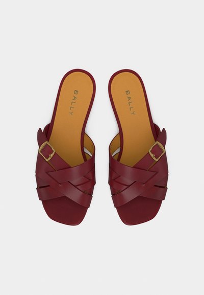 Paire de sandales en cuir bordeaux à enfiler avec des brides croisées, détail boucle dorée, semelles intérieures couleur beige et nom de la marque imprimé à l'intérieur.